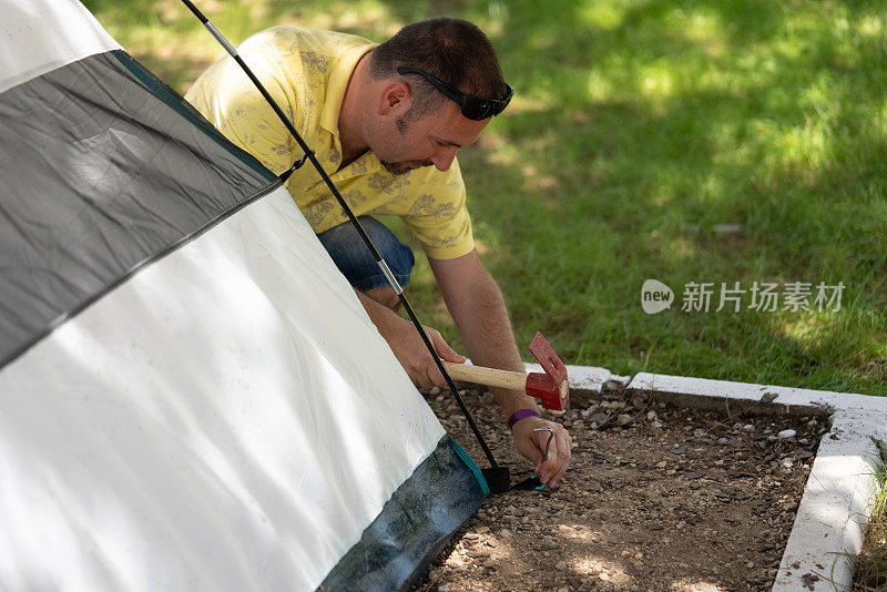 一个人用锤子把帐篷的钉子钉进地里