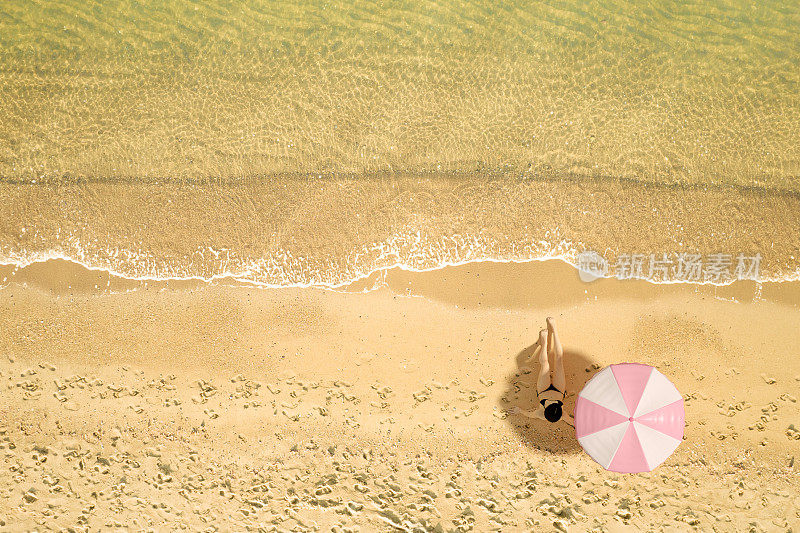 性感的女孩穿着黑色比基尼在海滩上日光浴，鸟瞰清澈的蓝绿色的大海，夏日度假旅行的背景