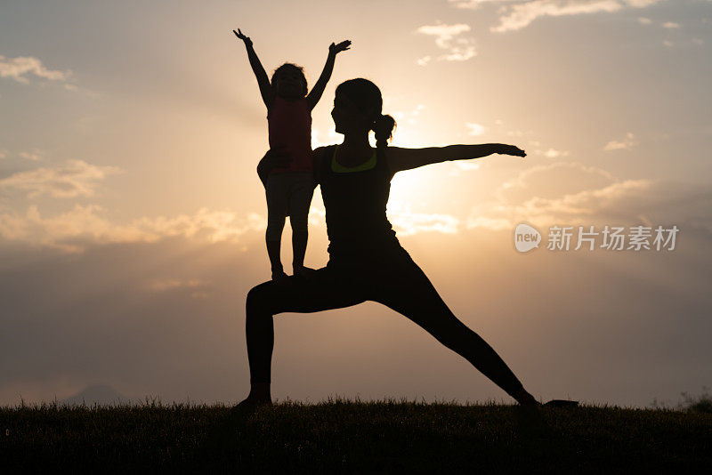 成年妇女和小女孩在夕阳下做瑜伽练习的剪影