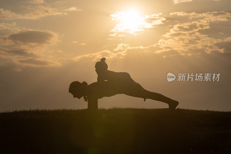 成年妇女和小女孩在夕阳下做瑜伽练习的剪影