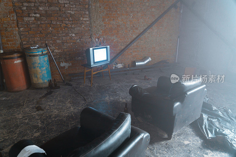 废弃的仓库，砖墙和两个皮革扶手椅指向旧电视与电视噪音