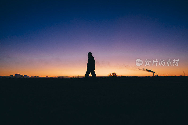 一名女子在傍晚散步，背景是煤和石油发电厂排放的废气