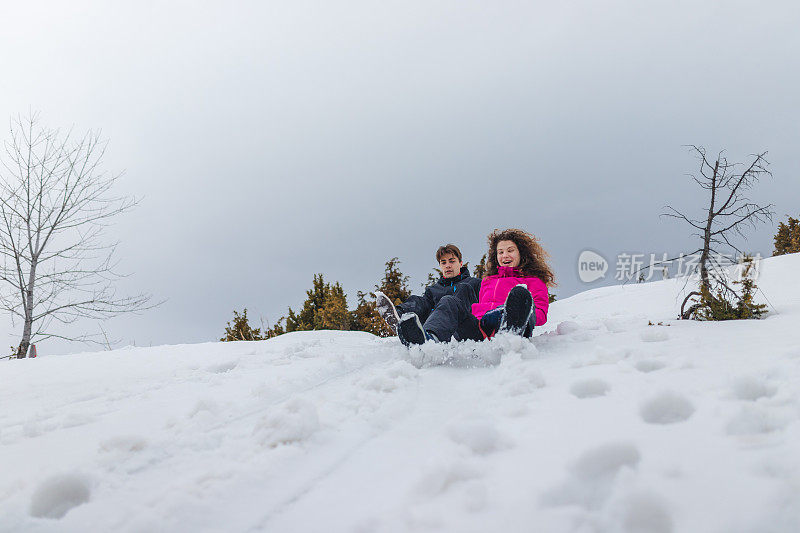 一对美丽的年轻夫妇坐在雪橇上从山上滑下来，在雪地里玩得很开心