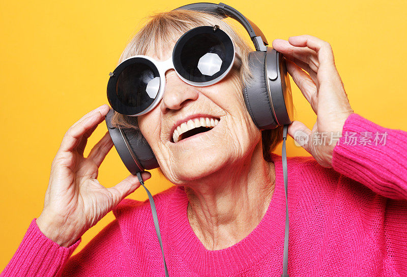 快乐的老妇人听音乐与耳机在黄色的背景。