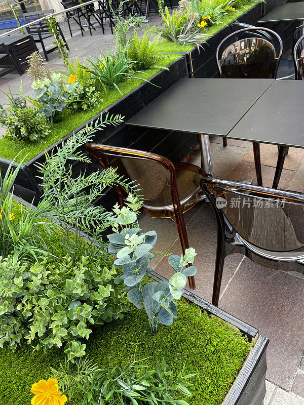 户外人行道咖啡馆的图像，餐厅桌椅，人造植物在凸起的木槽，重点放在前景
