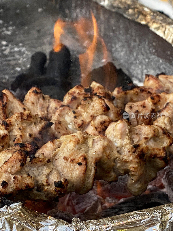 特写图像的鸡肉羊肉串，烧烤，腌鸡胸片木炭烤金属串，躺在一排排的热木炭烬火焰，集中在前景