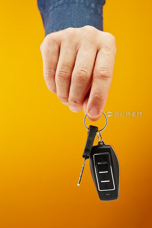 手握遥控汽车钥匙，可锁或开锁汽车，并打开黄色背景的汽车后备箱