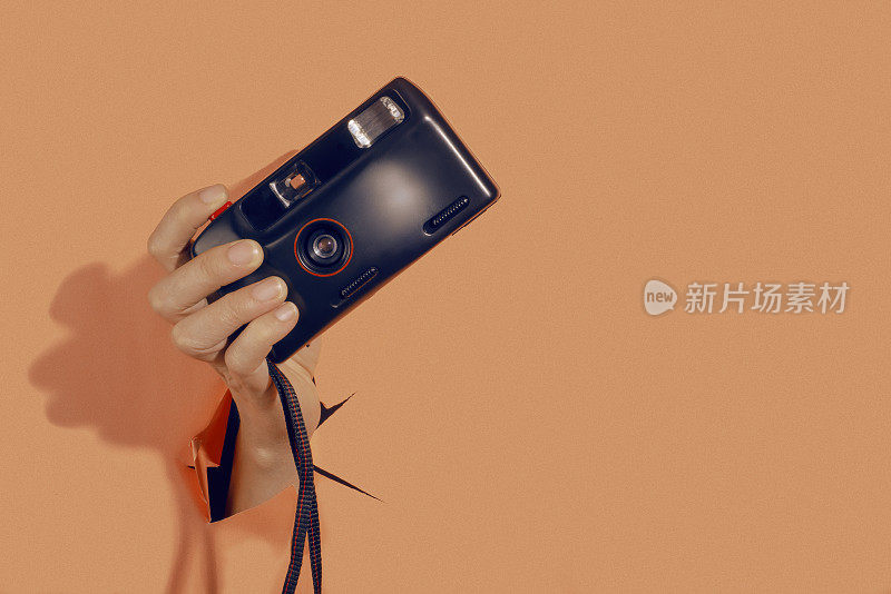 一位女性手拿着一台老式胶卷相机，背景是淡橙色