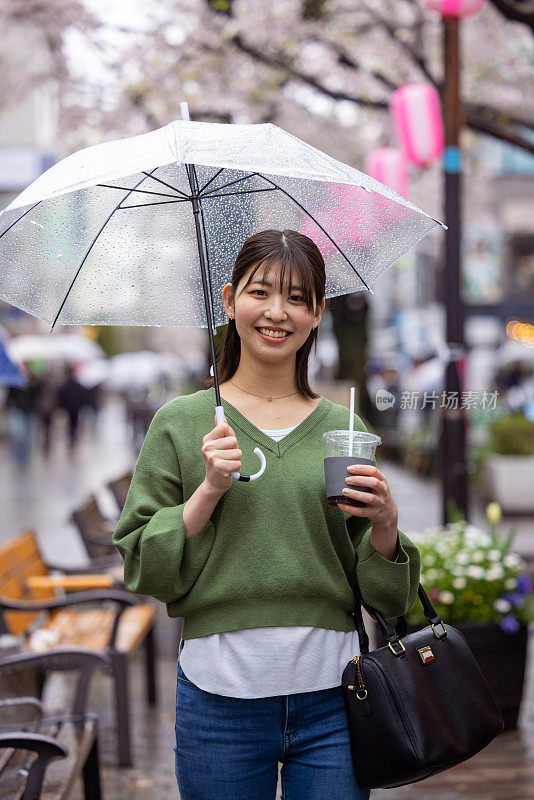 年轻女子站在樱花下的肖像在一个雨天的城市