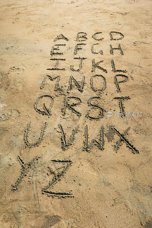 在阳光沙滩上用圆珠笔在沙滩上用块状大写字母写的图像，高架视图，重点在前景