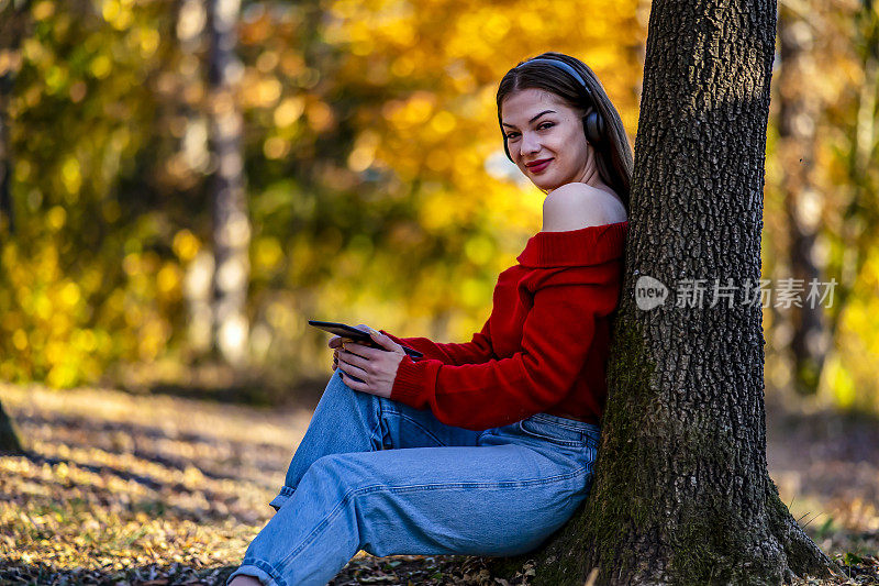 秋天的女人带着平板电脑和耳机在大自然中放松。