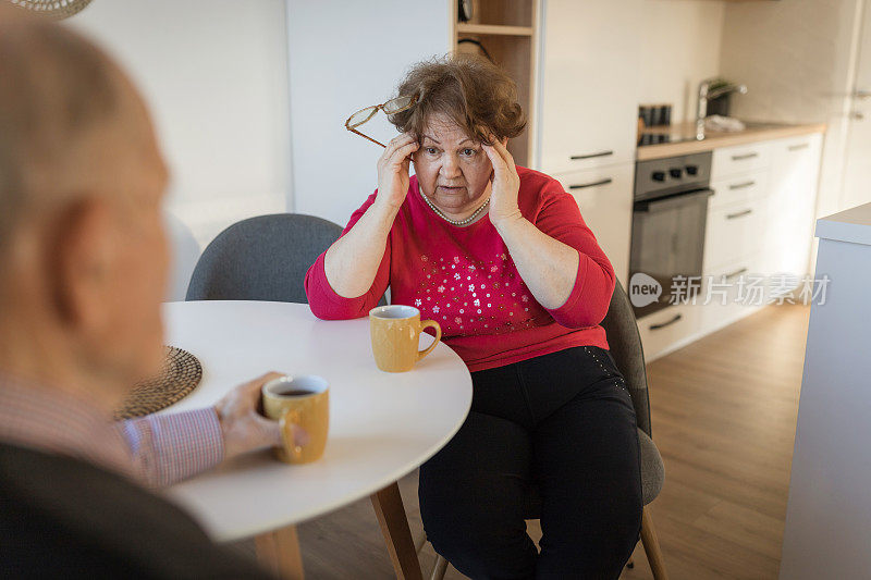 老年妇女在偏头痛期间按摩头部并进行交谈