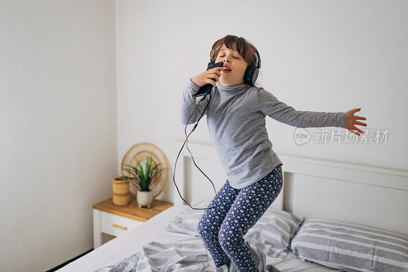 一个女孩闭着眼睛在卧室的床上跳着唱歌和听音乐