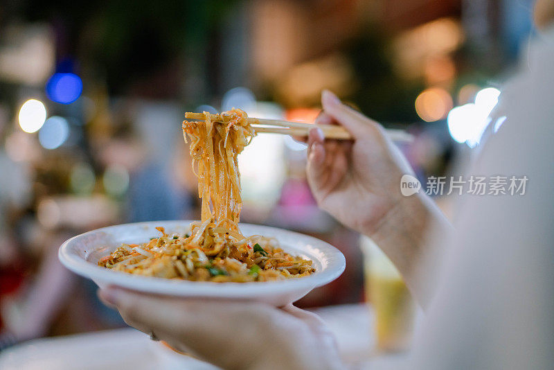 年轻的亚洲妇女在街边夜市吃晚餐。