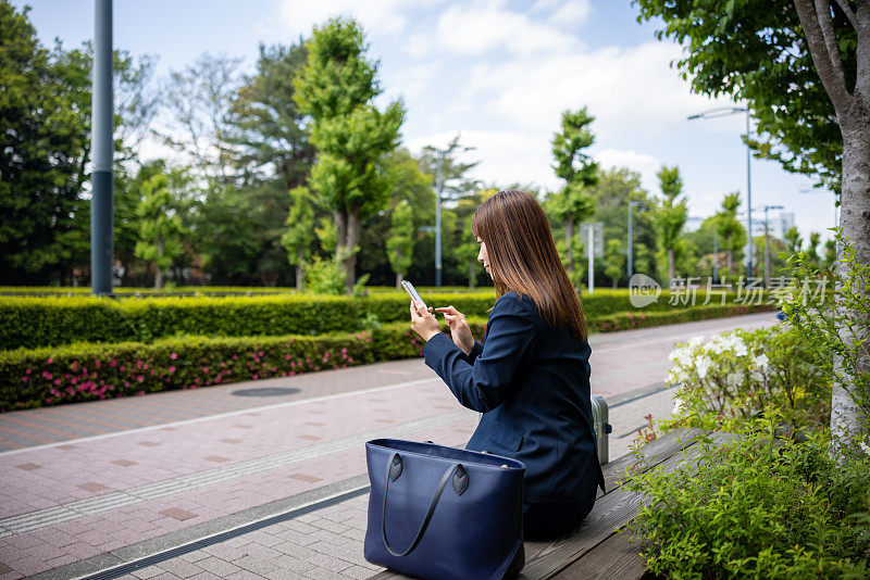 在城市里打电话的女商人，坐在长凳上，在商务旅行的后视图