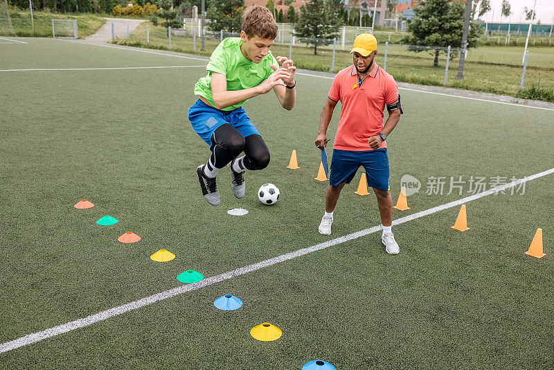 男孩正在接受黑人教练的个人足球训练，要求球员跳过障碍