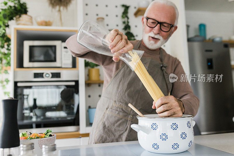 快乐的老人站在厨房柜台前，用勺子混合沙拉，同时在炉子上烹饪美味的健康餐。