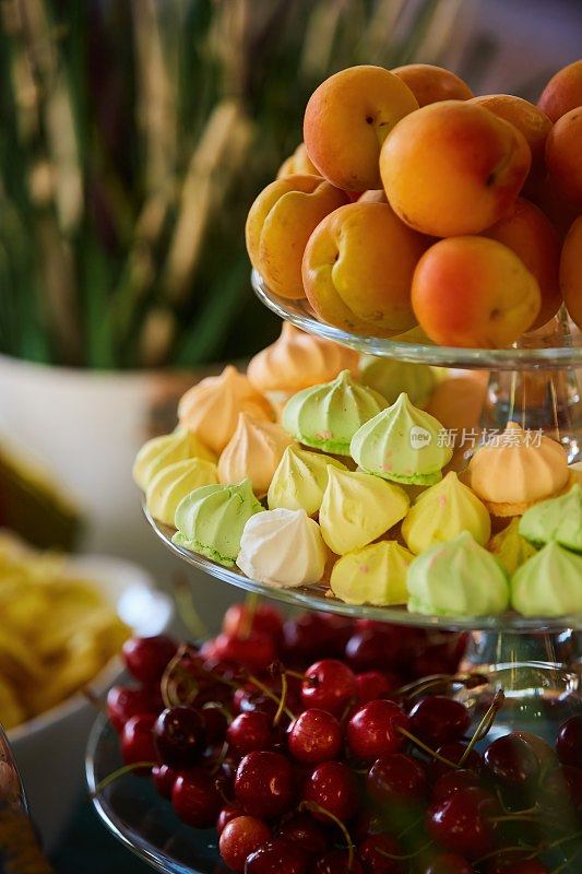 一个三层楼高的盘子，里面有水果和糖果。杏子，樱桃和松软的蛋白派