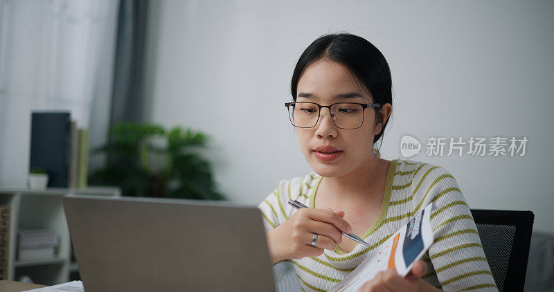 年轻的亚洲女性戴着眼镜，在家庭办公室里通过笔记本电脑进行视频会议