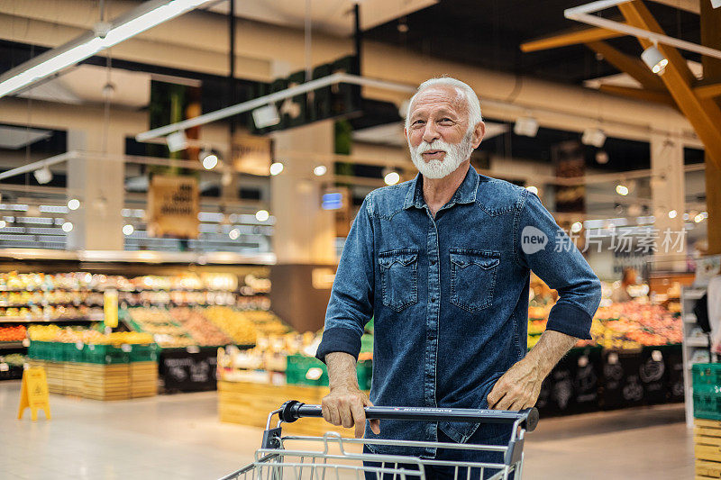 一个60多岁的英俊男人在每周的杂货店购物中穿过超市的过道，买了一些食物。