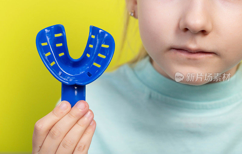 一个蓝色的牙印盘，背景是一个七岁女孩的嘴。为儿童制作牙颌印模的概念。矫正咬合及牙齿排列。牙科正畸学，黄色背景