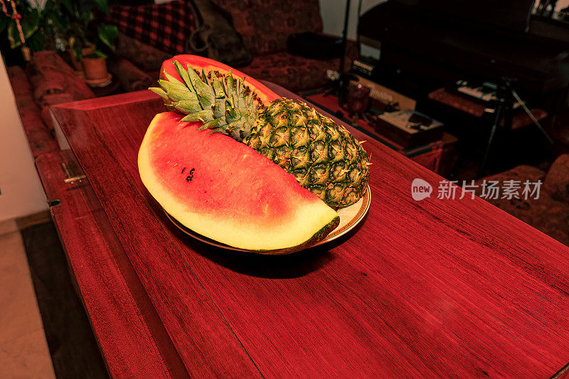 即食热带水果——一块西瓜和半个菠萝放在闪亮的红木桌上