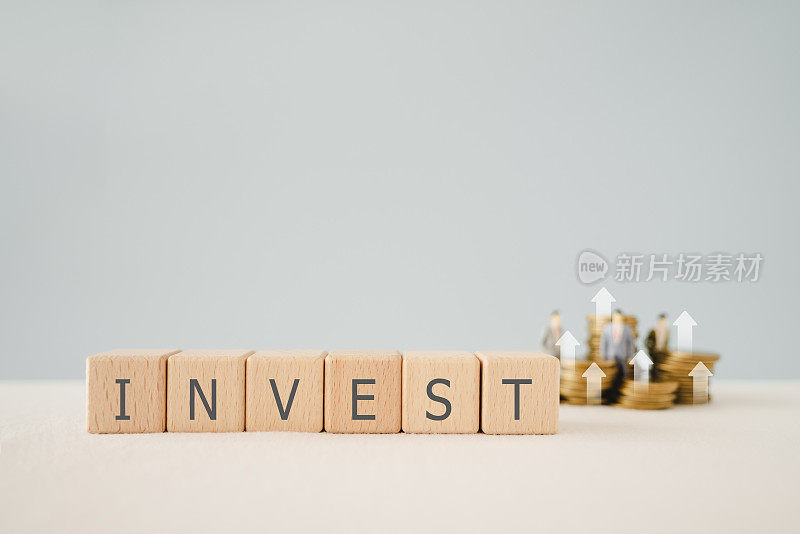 用模糊的硬币和商人微型堆叠在木制立方体块上投资文字。用于财务投资增长或投资决策的经营理念