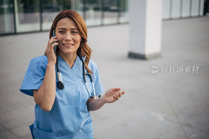 放松的女医生站在外面的医疗诊所前讲手机。