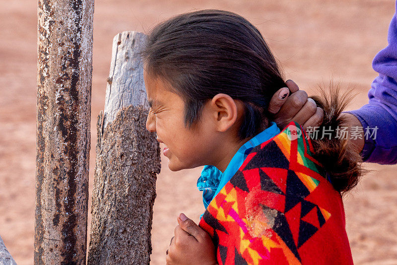 在亚利桑那州纪念碑谷的纳瓦霍印第安人保留地，小纳瓦霍男孩正在他的院子里梳头