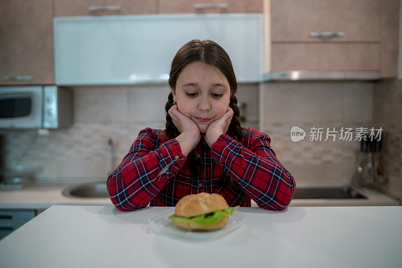 十几岁的女孩看着开胃的汉堡躺在她面前的桌子上