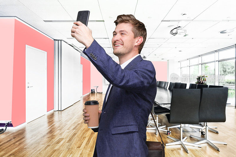 一名年轻男性在会议室拍照，肩包，手拿咖啡杯，使用智能手机