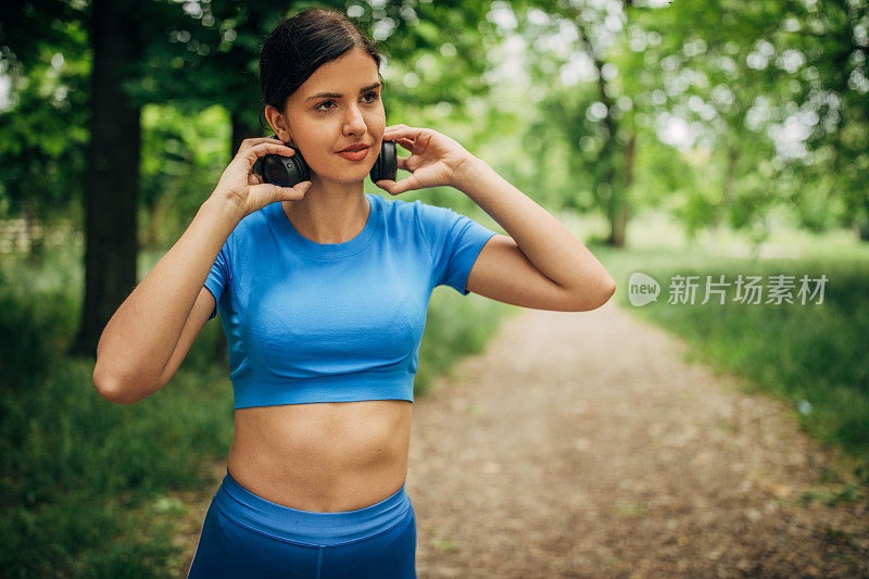 年轻漂亮的女人在公园里戴着耳机听音乐