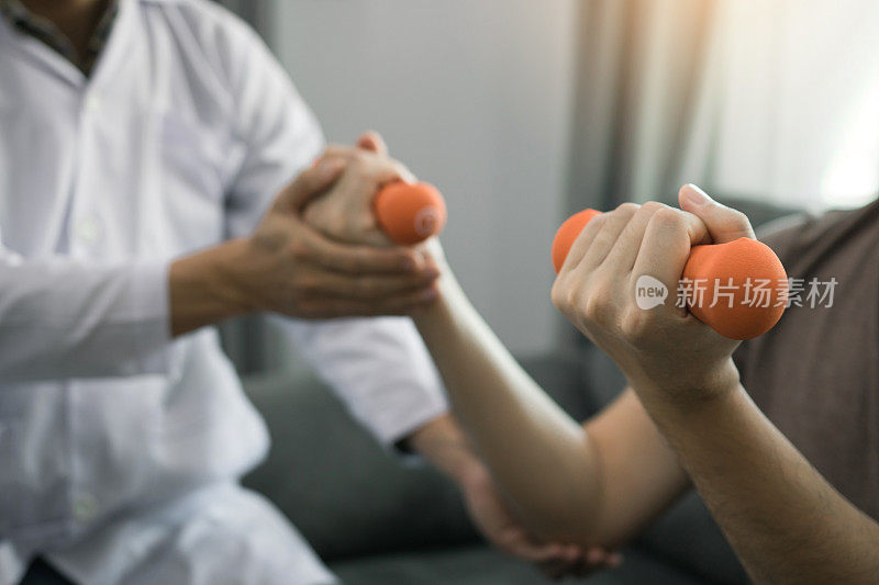 一名亚洲理疗师，在诊所里用重物帮助一个举哑铃的病人恢复。