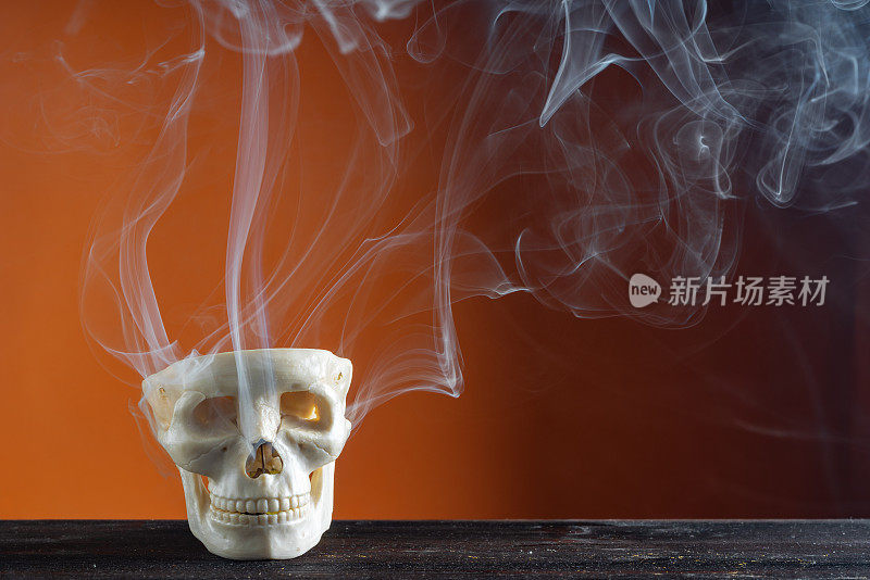 烟雾和人类头骨在橙色背景前的万圣节照片