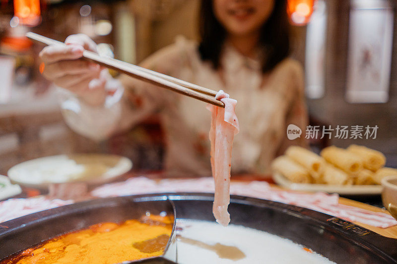 一位亚洲的中国妇女用火锅汤煮猪肉片