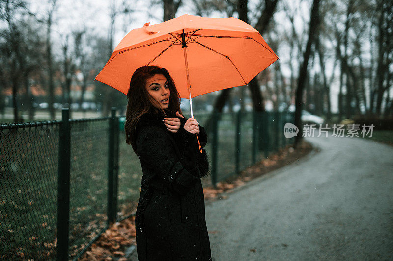 在一个下雪天，公园里拿着橙色雨伞的女人