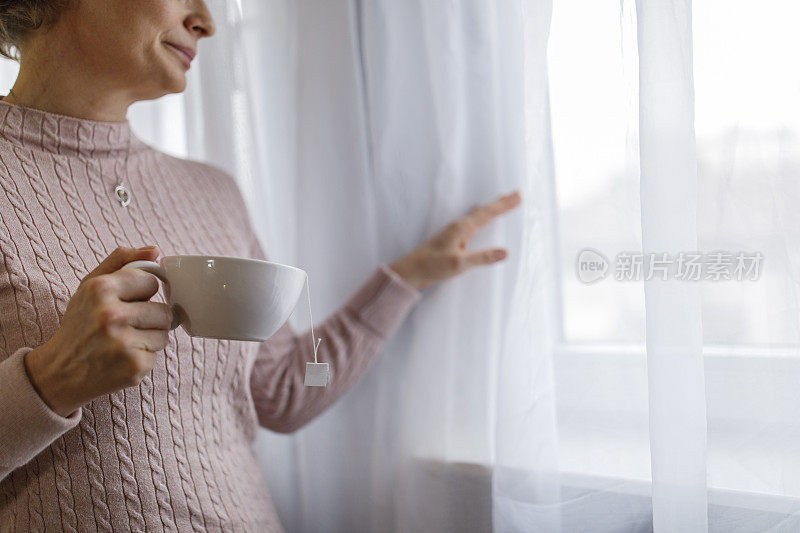 在窗边喝茶，看着窗外的女人的腹部