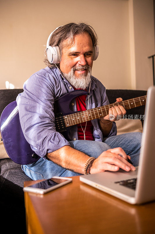 一个男人在客厅通过笔记本电脑学习电吉他。