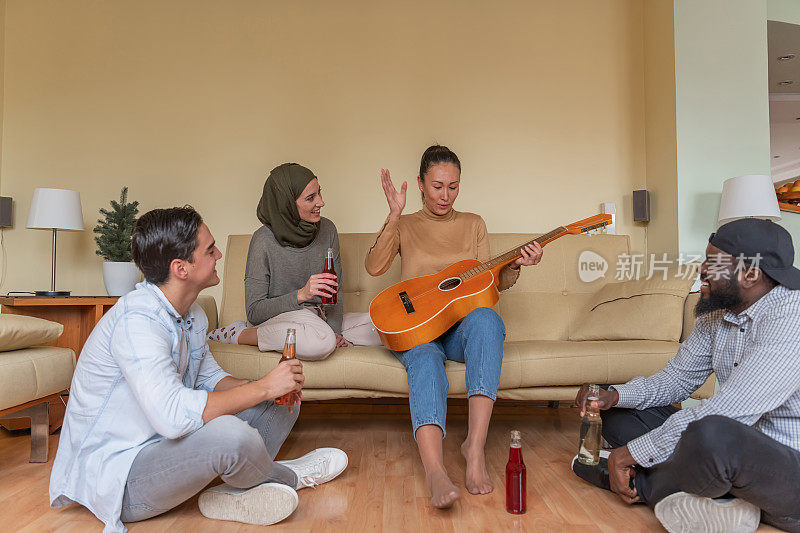 欢乐的多民族朋友们在现代公寓里放松，弹着原声吉他。