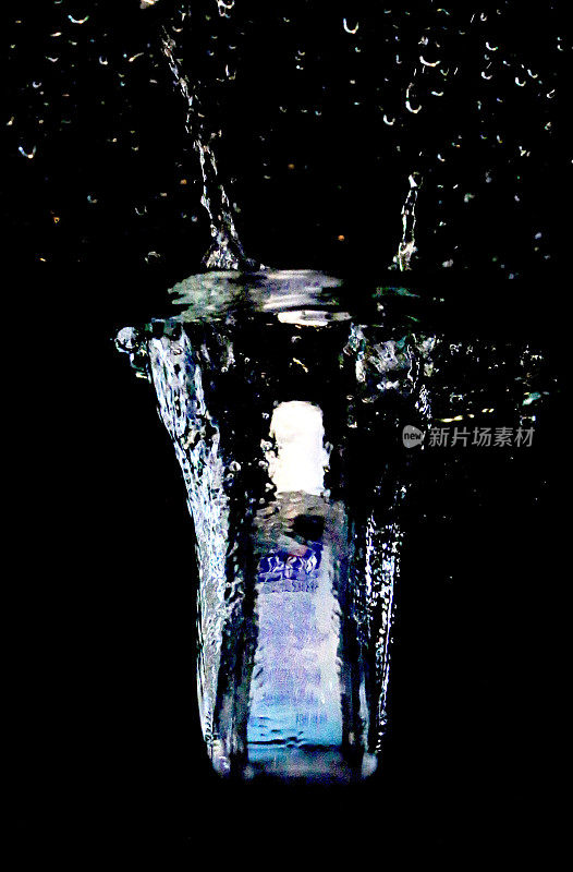 塑料瓶装洗手液掉进水中，泡沫和飞溅的水滴在黑色背景下，卫生概念