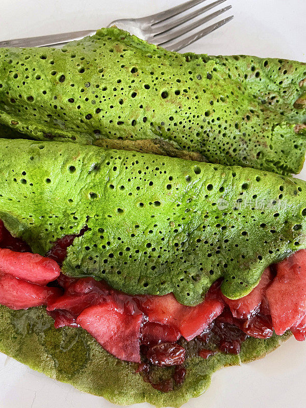 这是自制的绿色菠菜煎饼，配上苹果片和黑莓，用金属叉子放在白色盘子里，这是更健康的早餐概念，从高处看