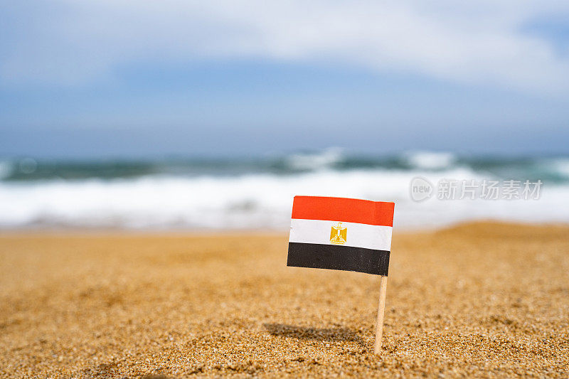埃及国旗的牙签形式在沙滩的沙子对面的海浪。旅游的概念