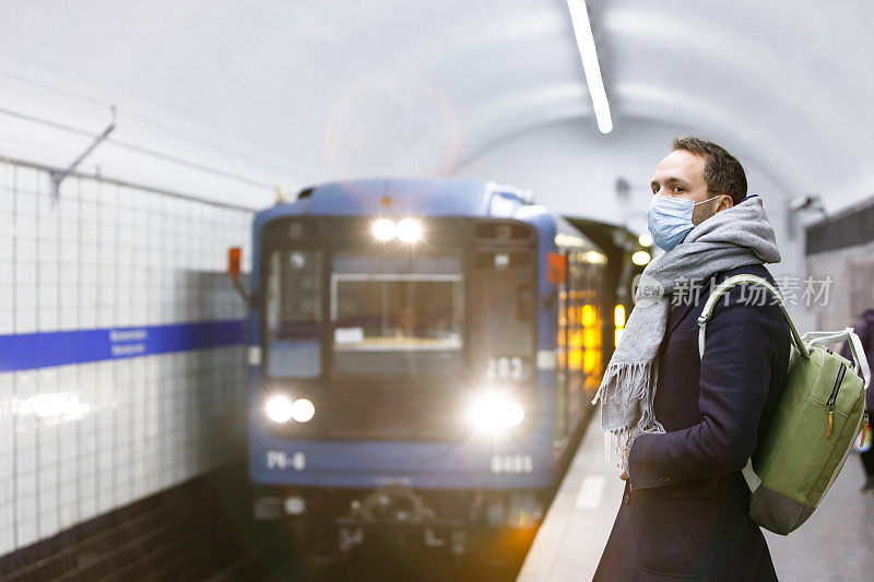 一名戴着防护口罩的男子在地铁站等火车。
