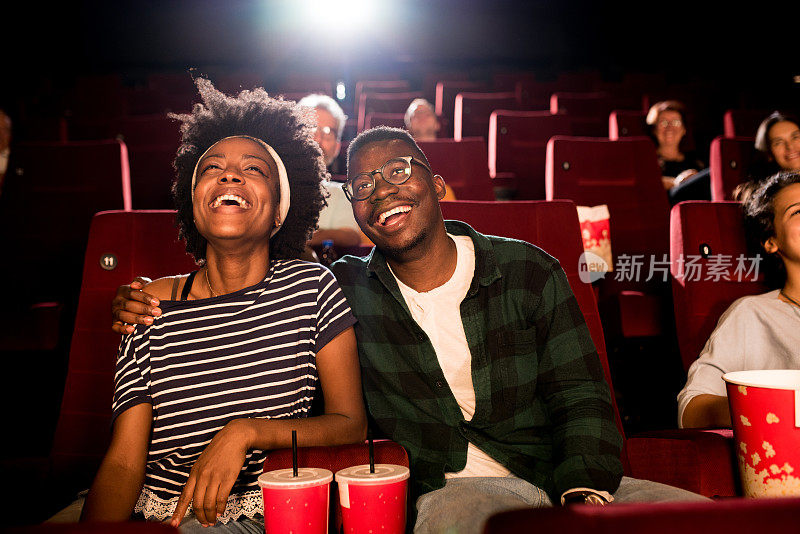 一对年轻的非洲裔美国夫妇在电影院看电影，玩得很开心