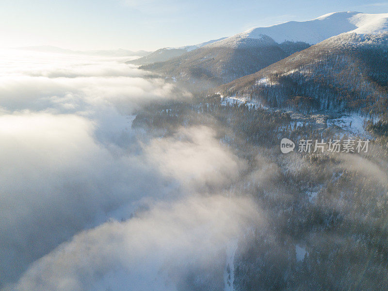 壮丽的日出在山上的空中拍摄。山与山之间的山谷被雾覆盖，被初升的太阳温暖的光线照亮。山上覆盖着天然的森林。