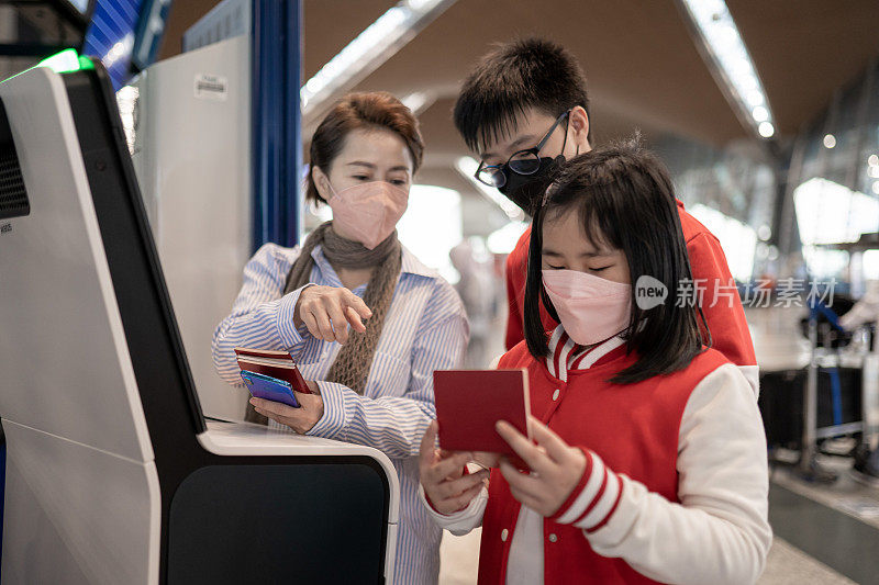带口罩的亚洲华人家庭在机场接受自动检票机检查。