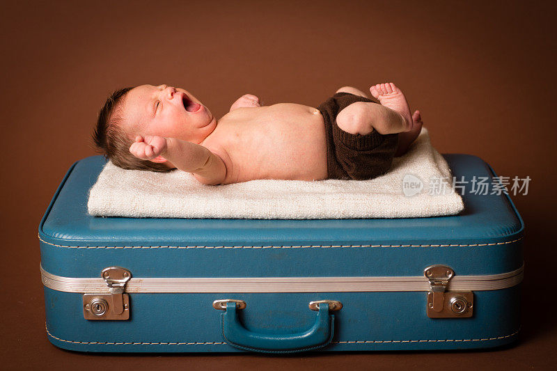 打哈欠新生儿躺在复古，蓝色行李箱