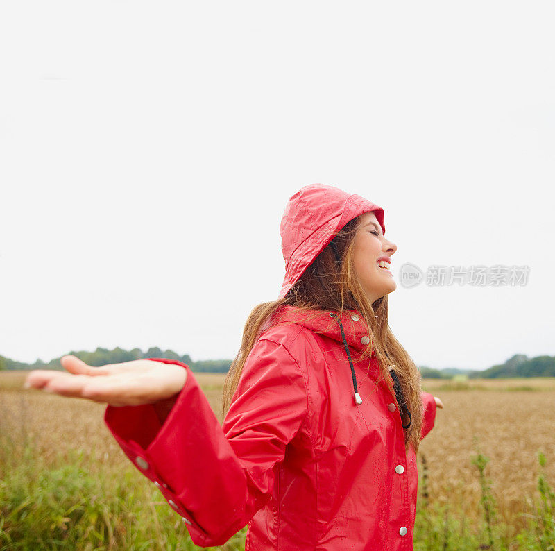 快乐的女人穿着雨衣，伸出双手，乡下