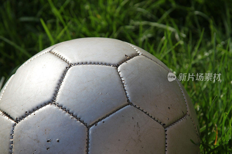 杂草丛生的草地上的破旧皮革足球(足球)