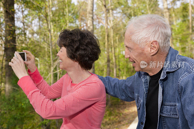 老年:活跃的老年夫妇在户外用智能手机拍照。